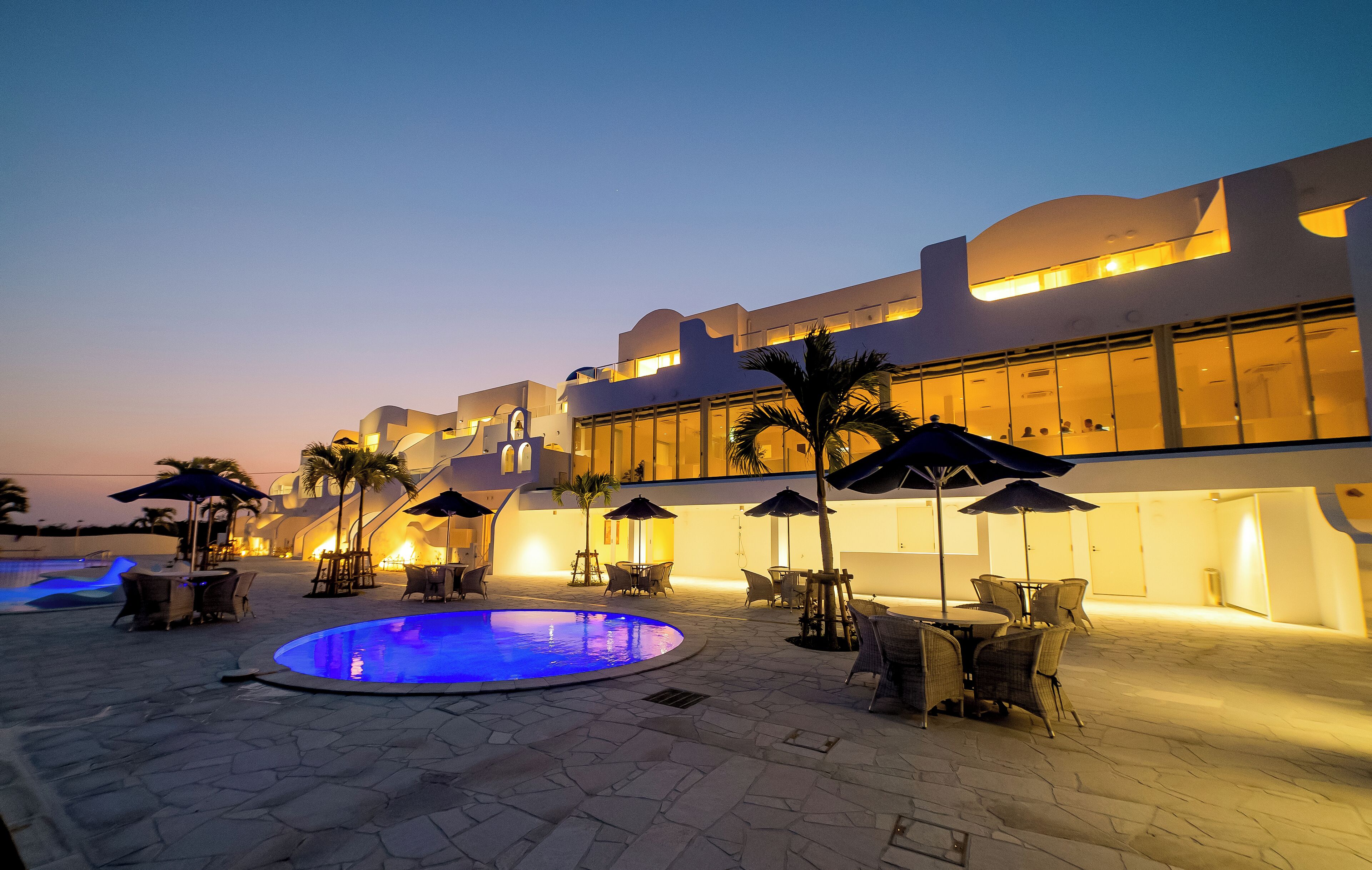 A modern hotel with a swimming pool, outdoor seating, and a well-lit facade.