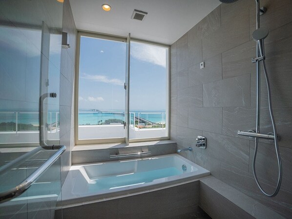 A modern bathroom with a glass-enclosed shower, a bathtub, and a view of the ocean.