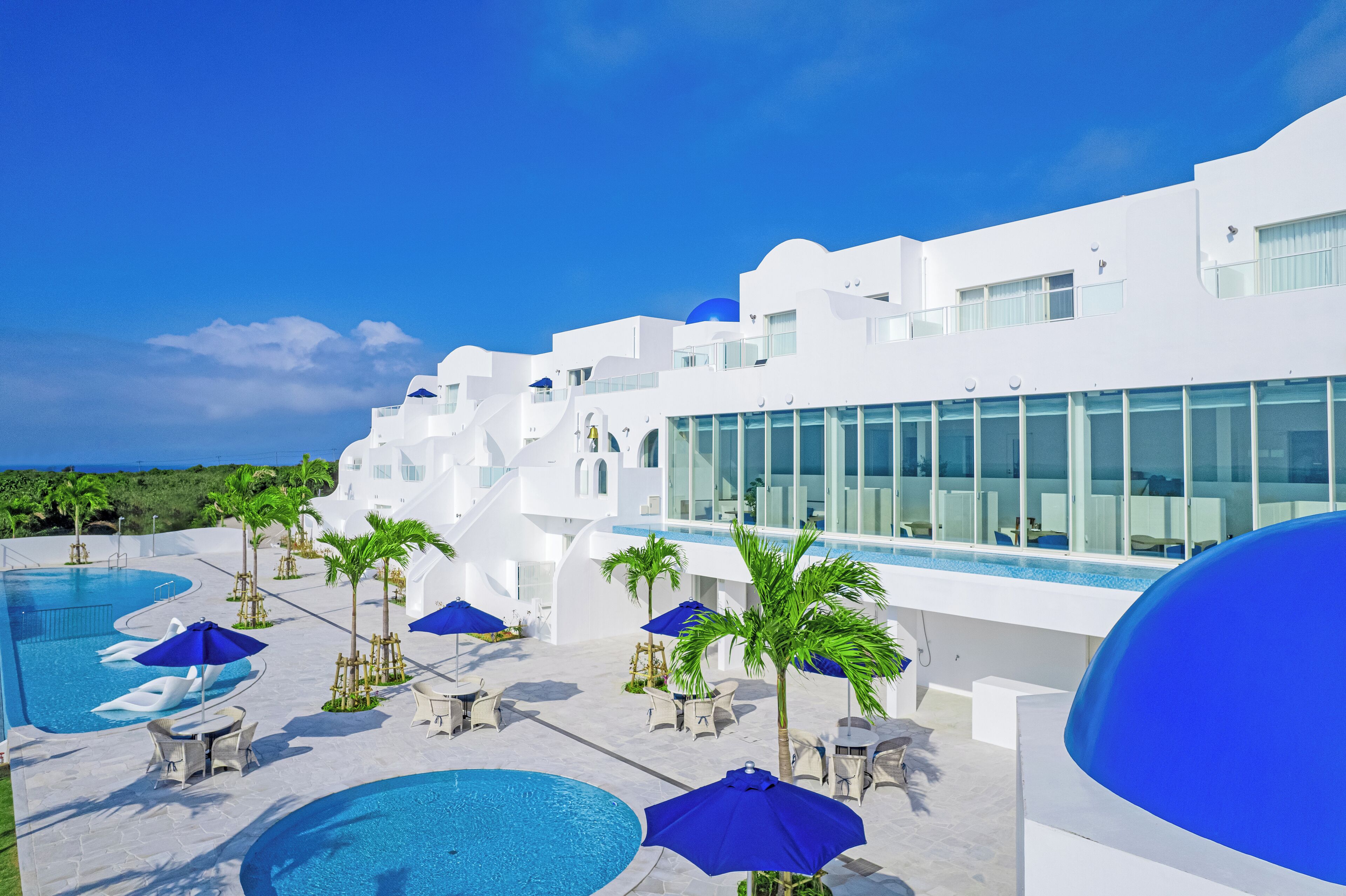 A modern hotel with a pool area, white architecture, and blue umbrellas.