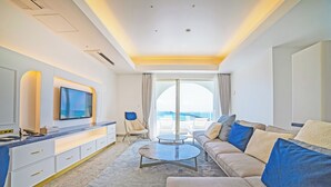 Une chambre d’hôtel moderne dotée d’un grand téléviseur à écran plat, d’un canapé, d’une table basse et offrant une vue sur la mer grâce à de grandes fenêtres.