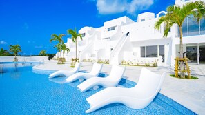 A modern pool area with white lounge chairs, palm trees, and a clear blue sky. - Santorini Hotel&Villas Miyakojima (Miyakojima)