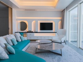Una sala de estar moderna con un sofá color turquesa, un sillón blanco, una mesa de centro redonda y un televisor de pantalla plana montado en la pared.