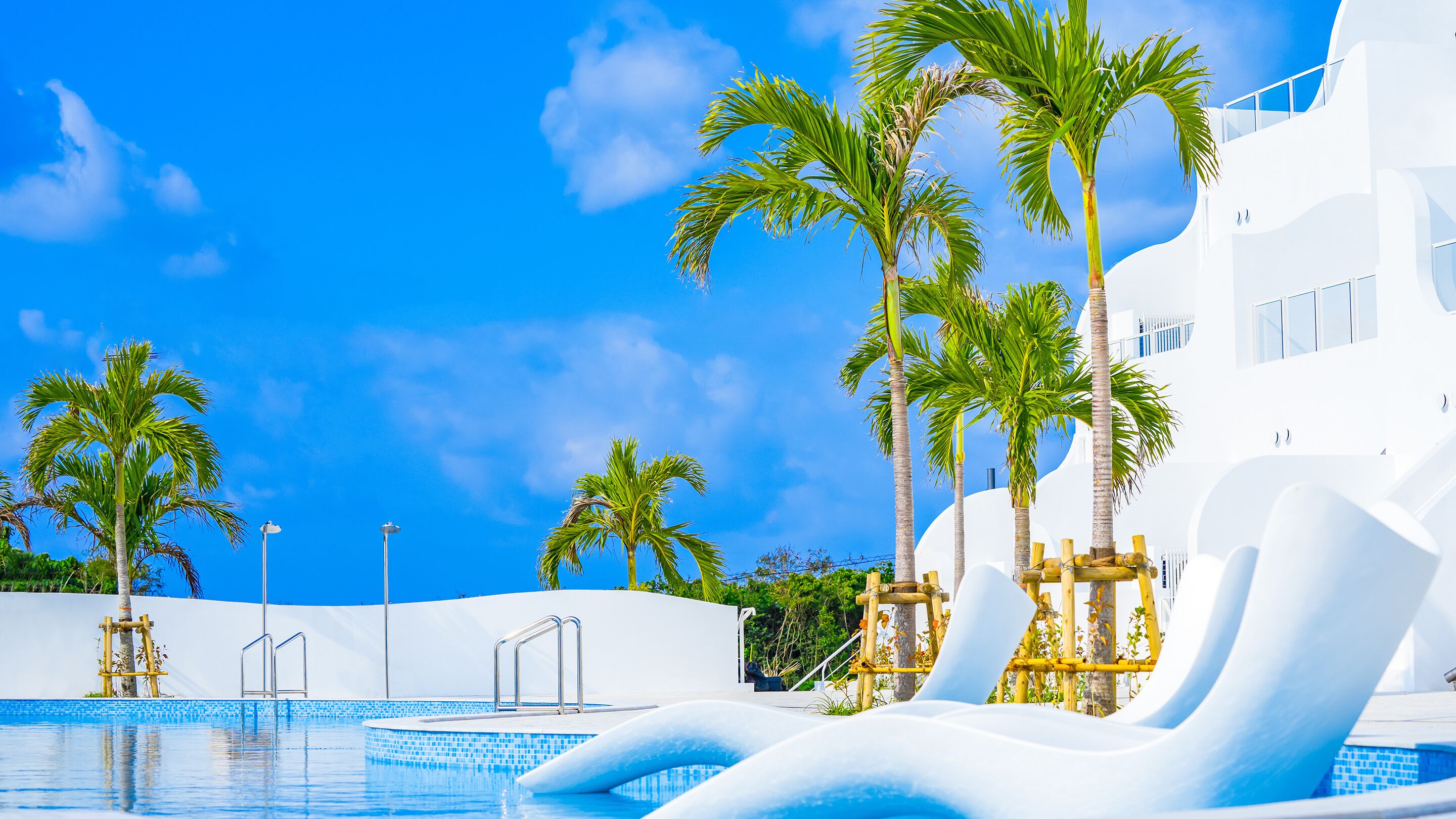 A pool area with palm trees, a water slide, and a white building.