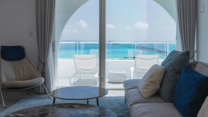 Un salon moderne doté d’une grande porte-fenêtre coulissante qui donne sur un balcon offrant une vue sur l’océan et un pont. On y trouve un canapé avec des coussins et une petite table ronde.