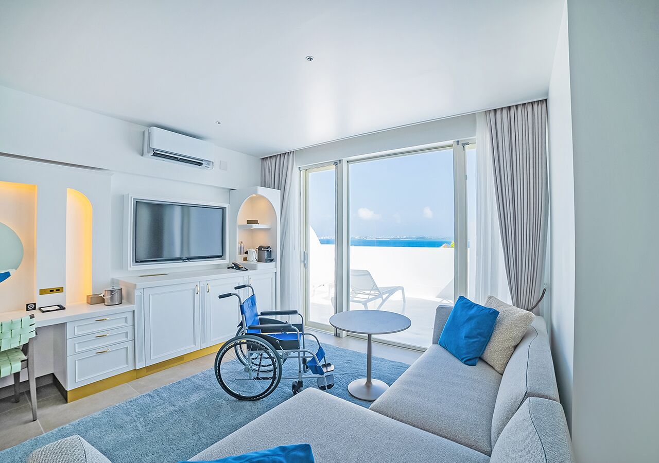 Een moderne hotelkamer met een rolstoel, een televisie, een zithoek en een balkon met uitzicht.