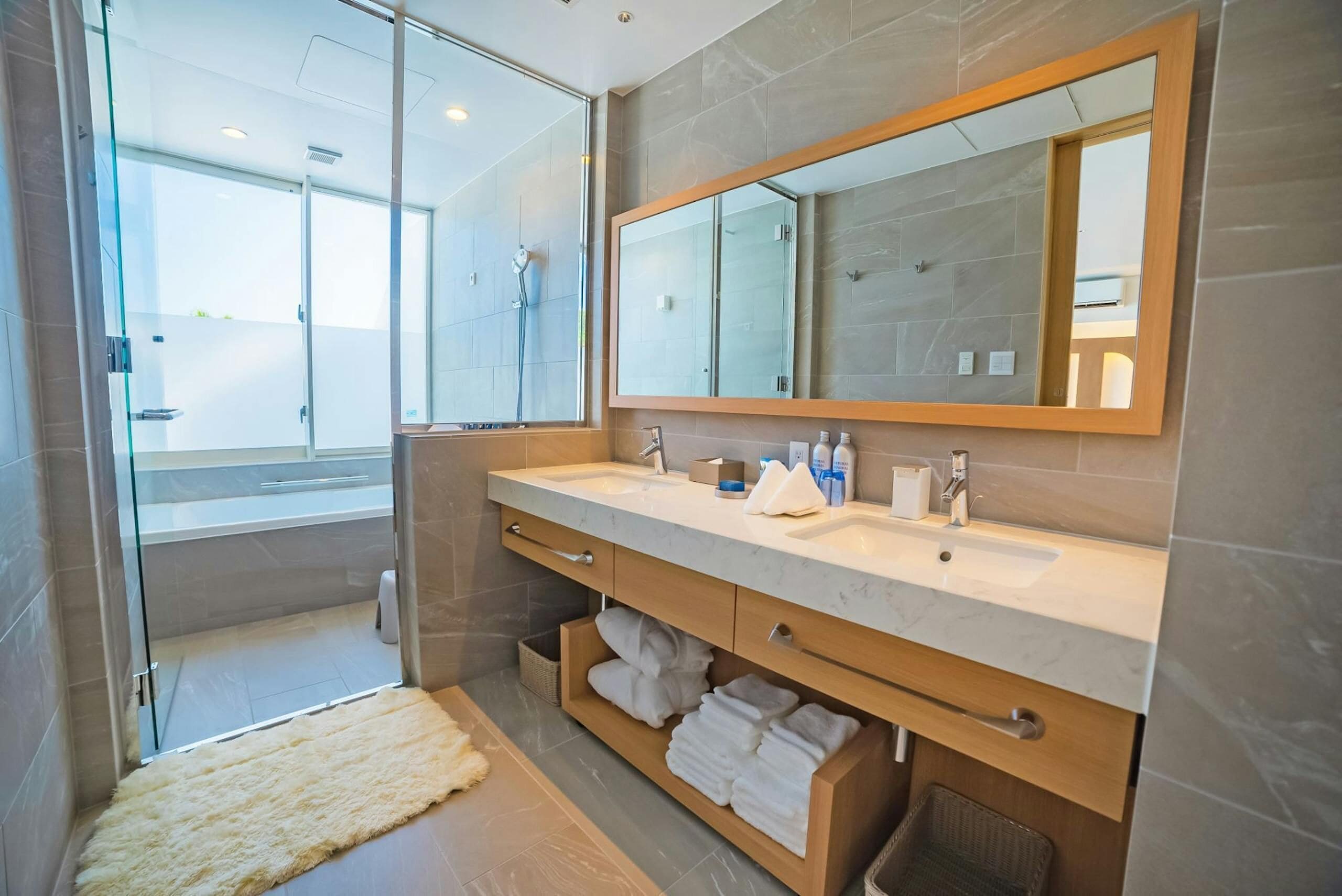 A modern bathroom with a glass shower enclosure, a large mirror, and a vanity with a marble countertop.