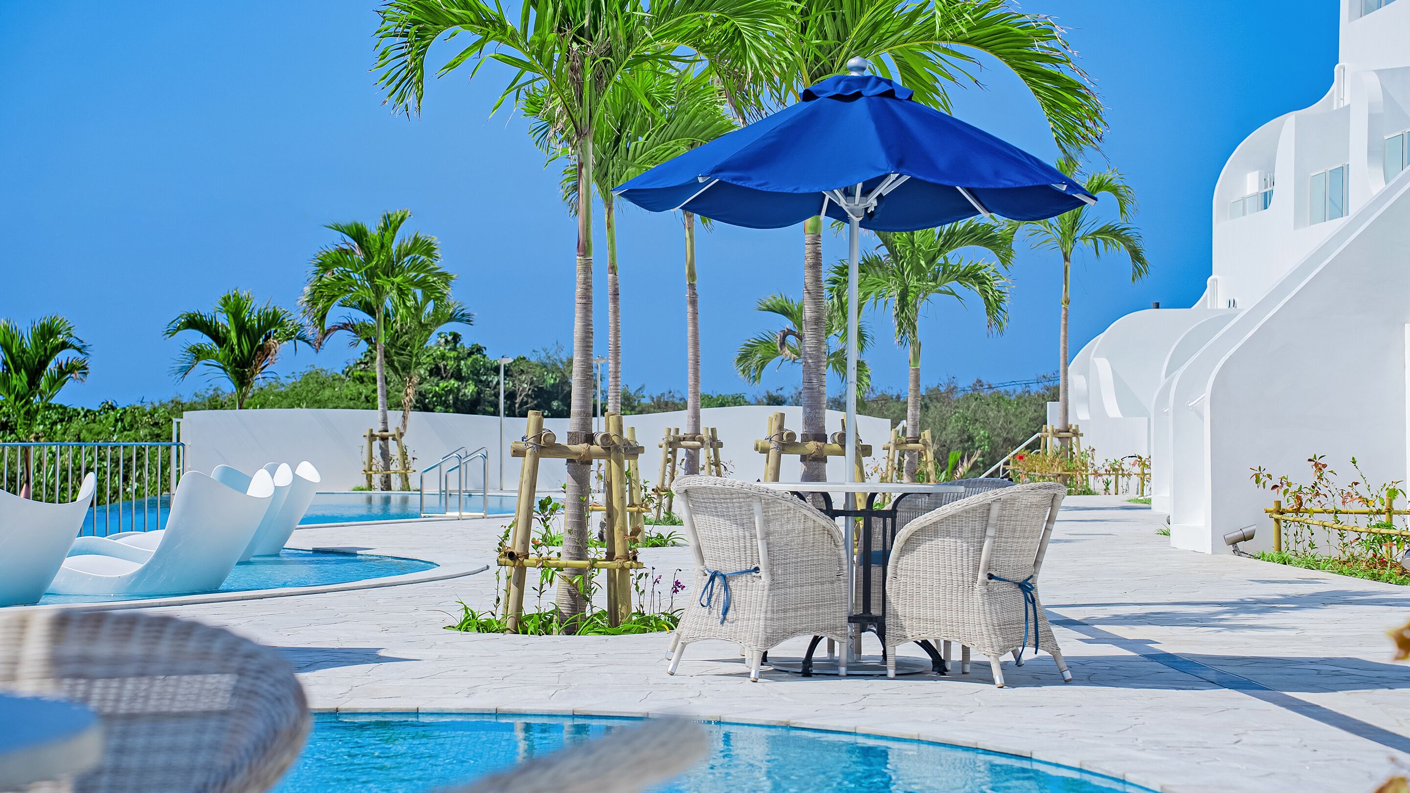 A poolside area with lounge chairs, a table, and a blue umbrella.