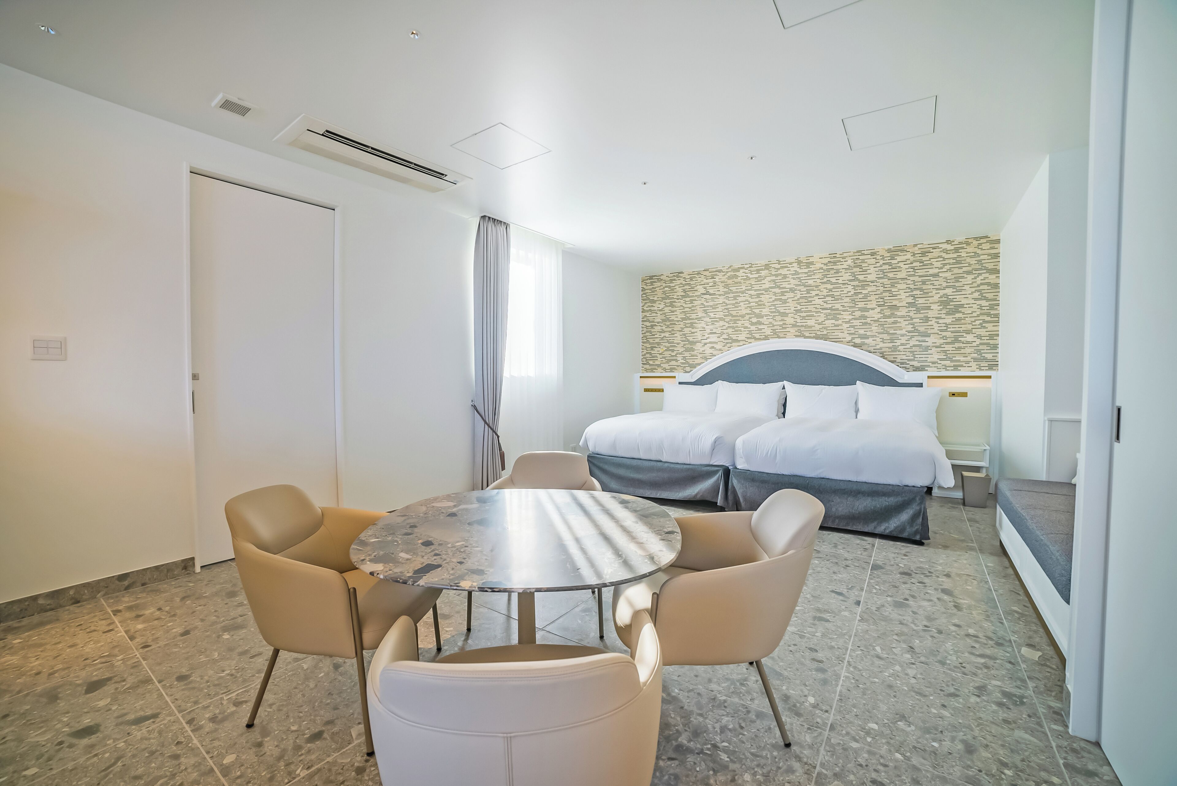 Habitación de hotel con cama, una mesa redonda con sillas, ventana con cortinas y pared con diseño.