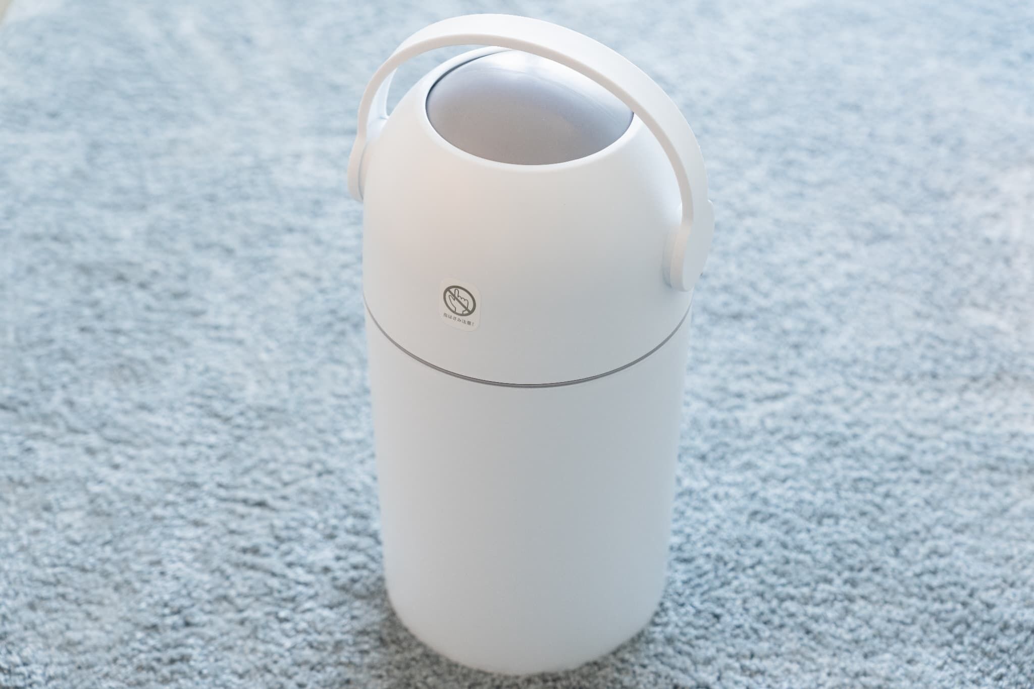 A white thermos with a handle on a textured surface.