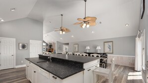 Una cocina amplia con una isla grande, muebles blancos y un ventilador moderno en el techo.