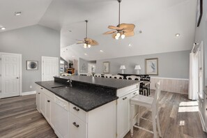 Una cocina amplia con una isla grande, muebles blancos y un ventilador moderno en el techo.