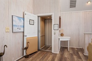Ein Flur mit Holzboden, einer weißen Tür, einem gerahmten Bild, einem kleinen Tisch mit Lampe und einer dekorativen Vogelplastik.