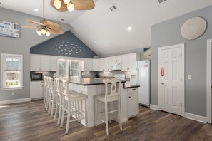 Eine moderne Küche mit weißen Schränken, einer zentralen Kochinsel mit Barhocker, einem Deckenventilator und einer Mikrowelle.