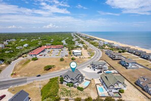 Vue aérienne d’une zone résidentielle côtière, avec des maisons, une plage et une route.