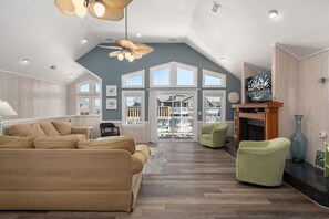 A spacious living room with a high ceiling, large windows, a fireplace, and a television. - Sea You Soon: Semi-Oceanfront, Private Pool, Dog Friendly, Hot Tub and Game Room! (Southern Shores)