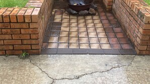 Un foyer extérieur en briques, doté d’une grille en métal, entouré d’un muret en briques et installé sur une terrasse en béton.