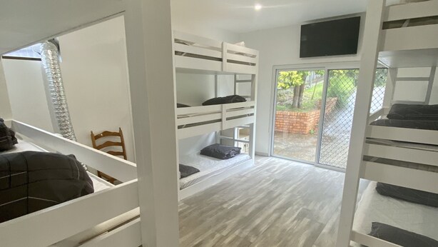 Une chambre moderne avec des lits superposés, un téléviseur à écran plat fixé au mur et une grande porte-fenêtre coulissante donnant sur un espace extérieur.