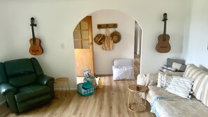 Un salon spacieux avec un canapé vert, un canapé à motifs et un plancher en bois. Deux guitares sont accrochées aux murs, et une petite table avec une lampe se trouve dans la pièce.