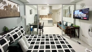 Une chambre moderne équipée d’un lit, d’une télévision et d’un coin repas, visible à travers une porte vitrée.