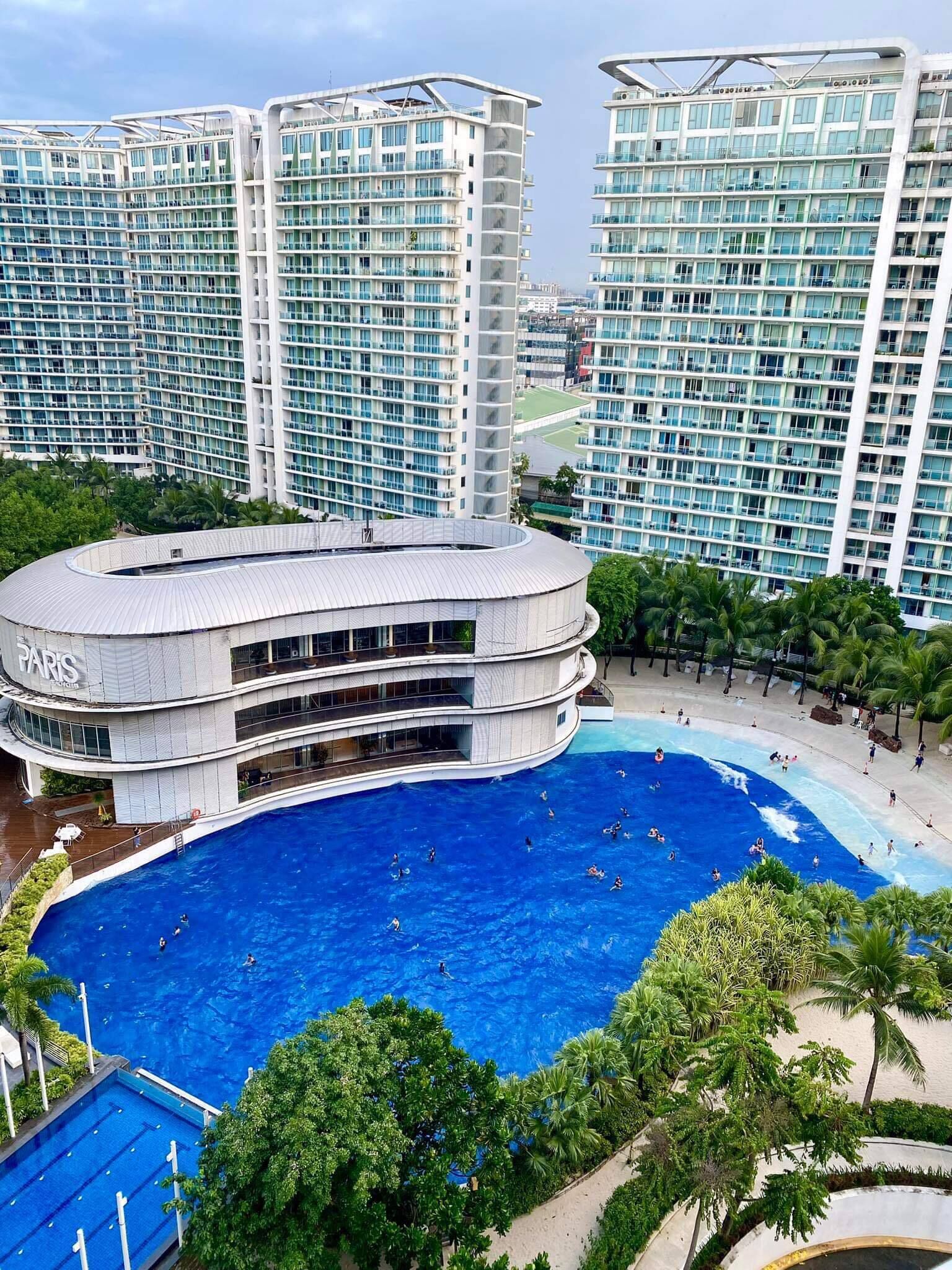 Um hotel moderno com uma ampla piscina central rodeada por vegetação exuberante e edifícios altos.