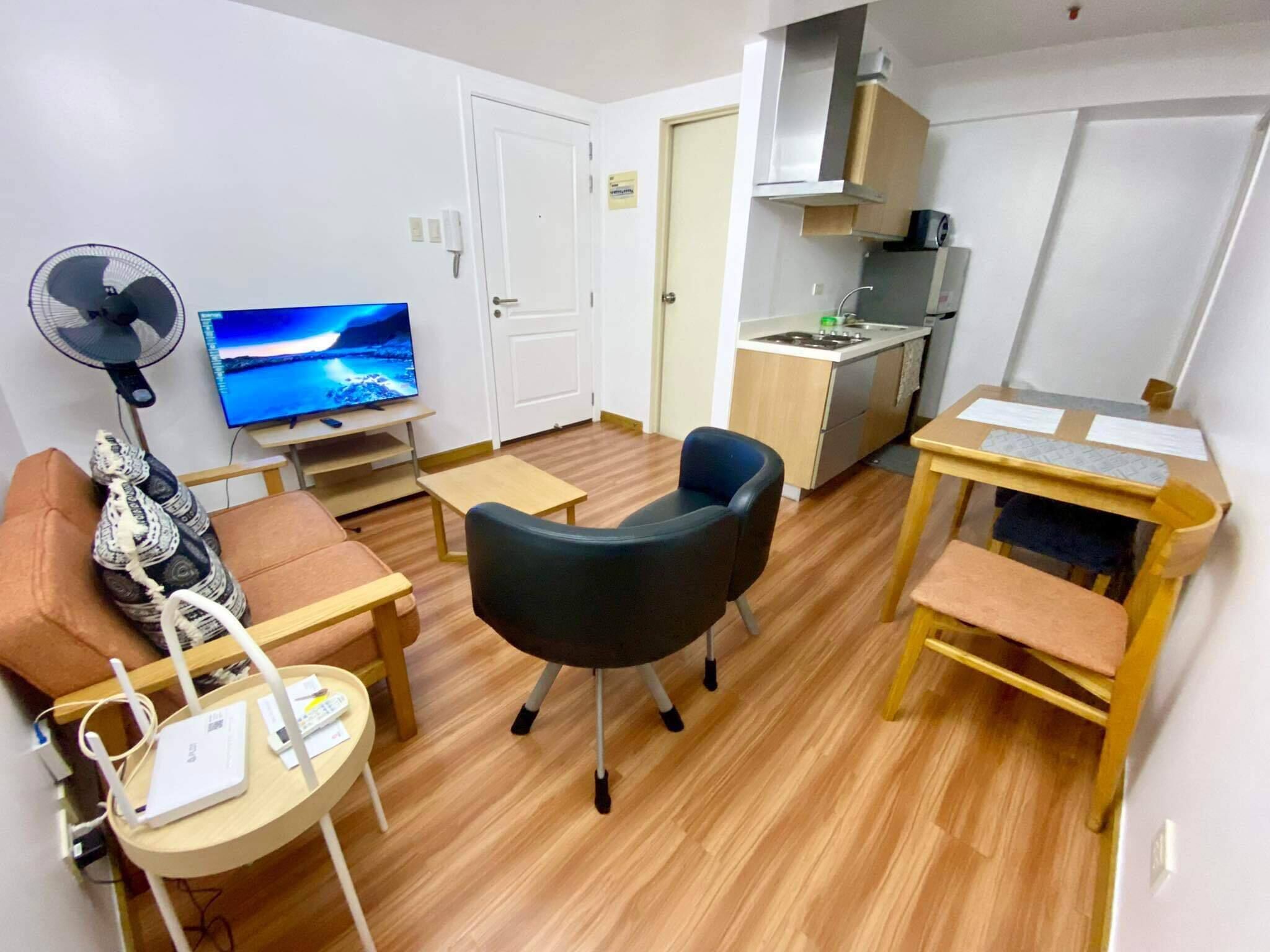 Un espace de vie compact comprenant une télévision, un ventilateur, un canapé, une table à manger et un coin cuisine.