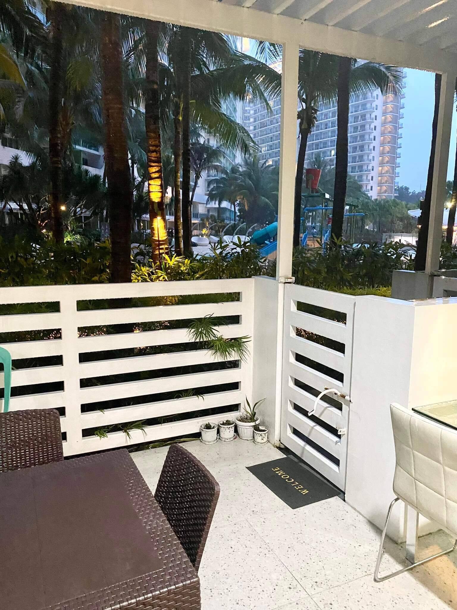 Un patio al aire libre con una mesa, sillas, cerca blanca y plantas en macetas.