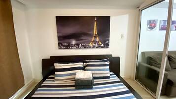 Une chambre à coucher avec un lit doté de draps à rayures, une grande fenêtre et un tableau représentant la Tour Eiffel accroché au mur.
