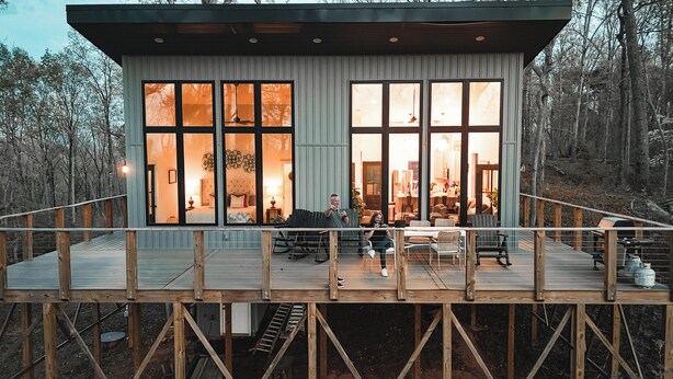 En moderne hytte med store vinduer, en terrasse og et spiseområde.
