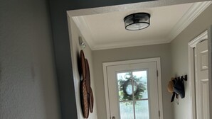 A hallway with a white door, a ceiling light fixture, and a wall-mounted hat rack.