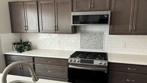 A kitchen with dark wooden cabinets, a stainless steel sink, a microwave, and a gas stove.