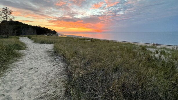 Un sentier qui longe la plage et mène à l’océan, avec un coucher de soleil en arrière-plan.