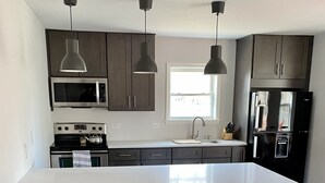 Une cuisine moderne dotée d’un grand îlot central, de chaises en bois, d’un four à micro-ondes, d’une cuisinière et d’un réfrigérateur.