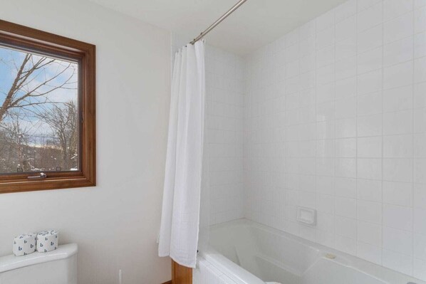 A bathroom with a bathtub, a window with a view of trees, and a toilet.