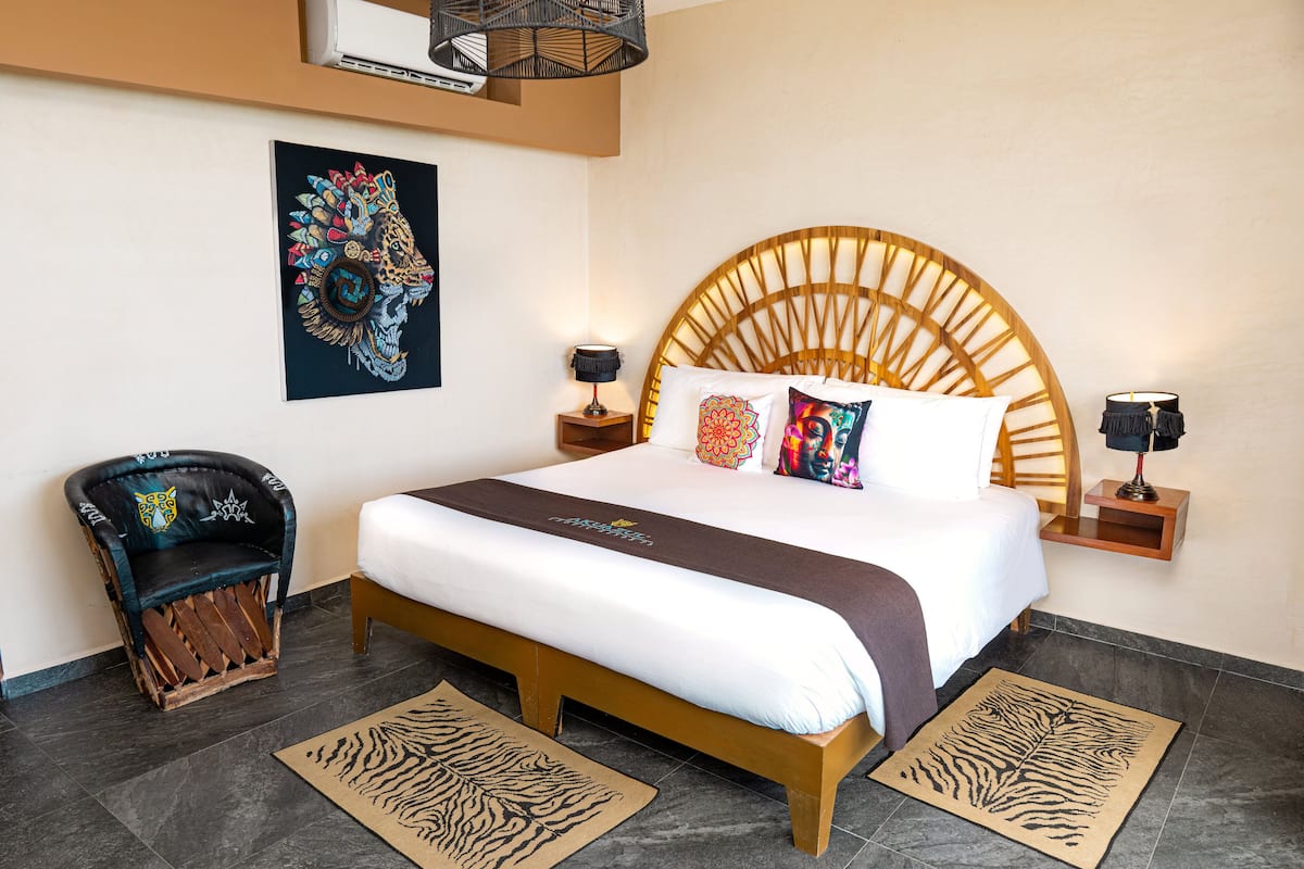 Een hotelkamer met een groot bed, hoofdeinde, twee nachtkastjes, een stoel en een kunstwerk aan de muur.