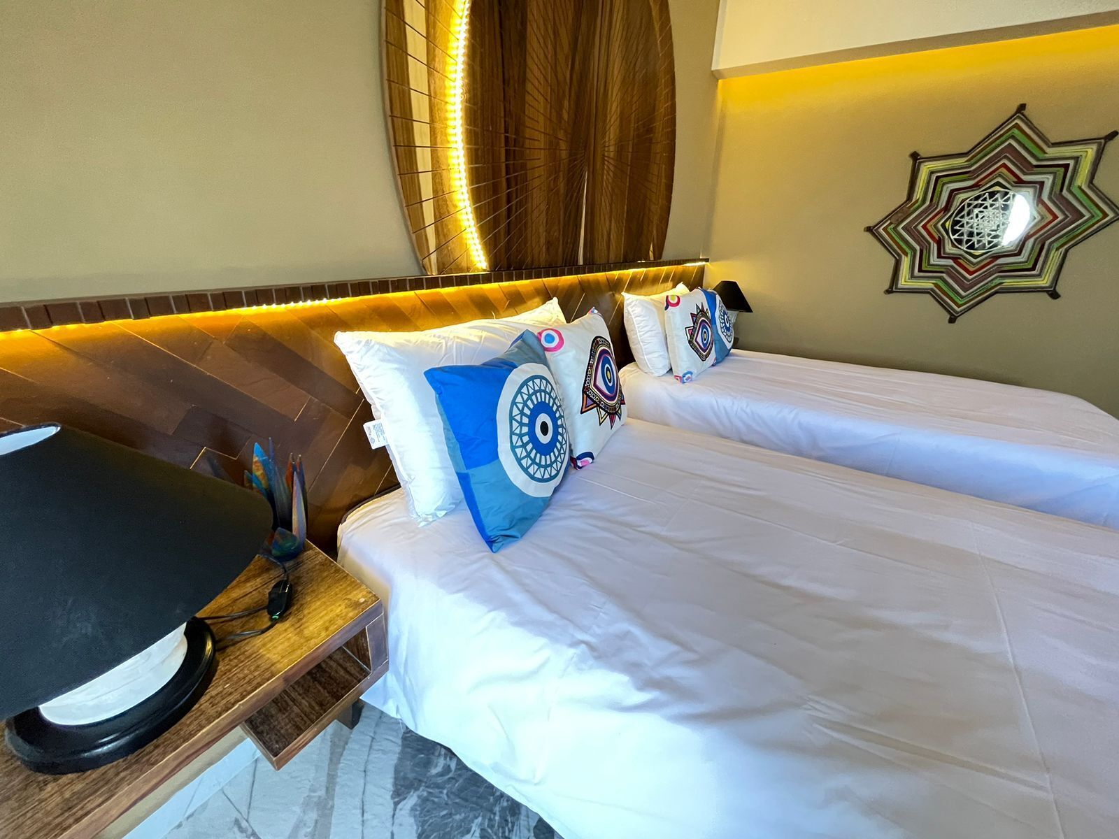 Una habitación de hotel con cama, mesita de noche, lámpara, almohadones decorativos y una obra de arte en la pared.