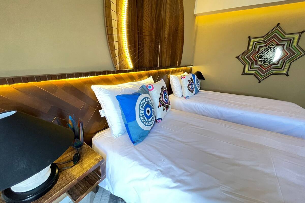 Een hotelkamer met een bed, nachtkastje, lamp, decoratieve kussens en een kunstwerk aan de muur.