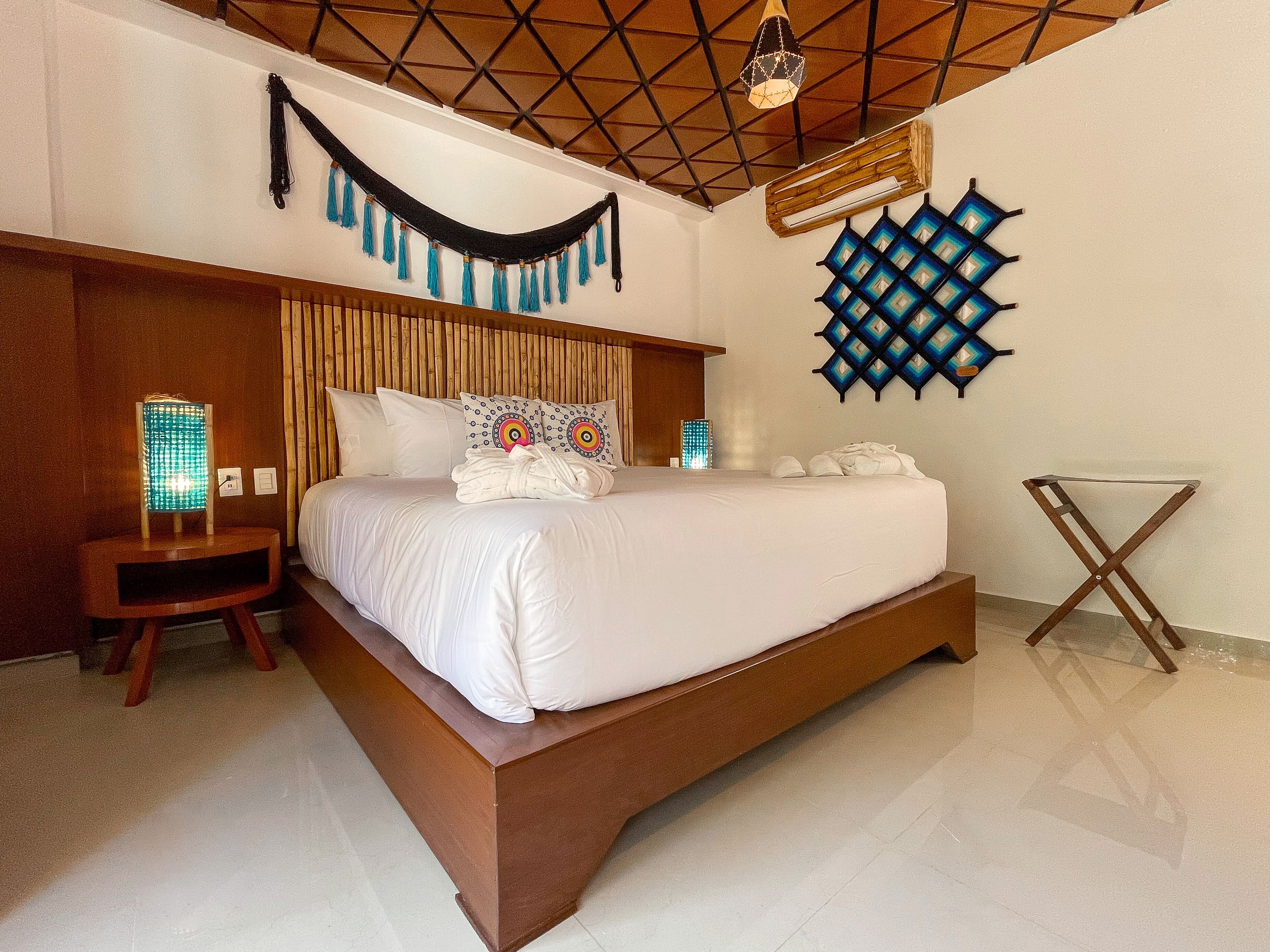 A modern hotel room with a large bed, wooden headboard, and a unique ceiling design.