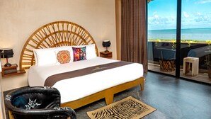 Une chambre d’hôtel avec un grand lit, une tête de lit en bois, une vue sur l’océan, un balcon avec des sièges et un tapis à motifs zébrés.