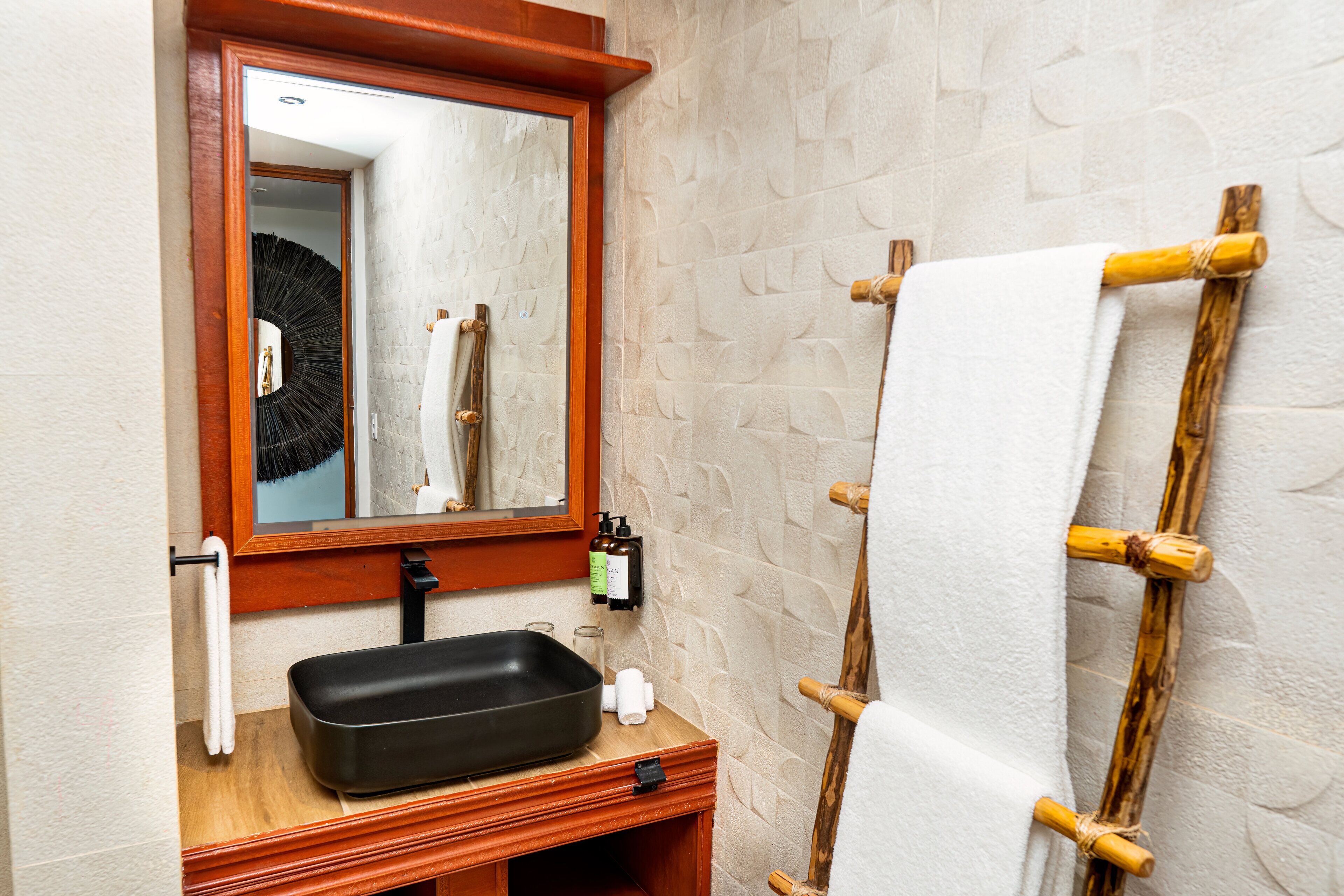 Une salle de bain avec un meuble-lavabo en bois, un évier noir, un miroir et un porte-serviettes.