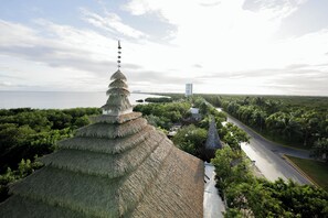 A traditional multi-tiered structure with a thatched roof, surrounded by lush greenery and a road. - Akuazul Resorts Adults Only (Cancun)