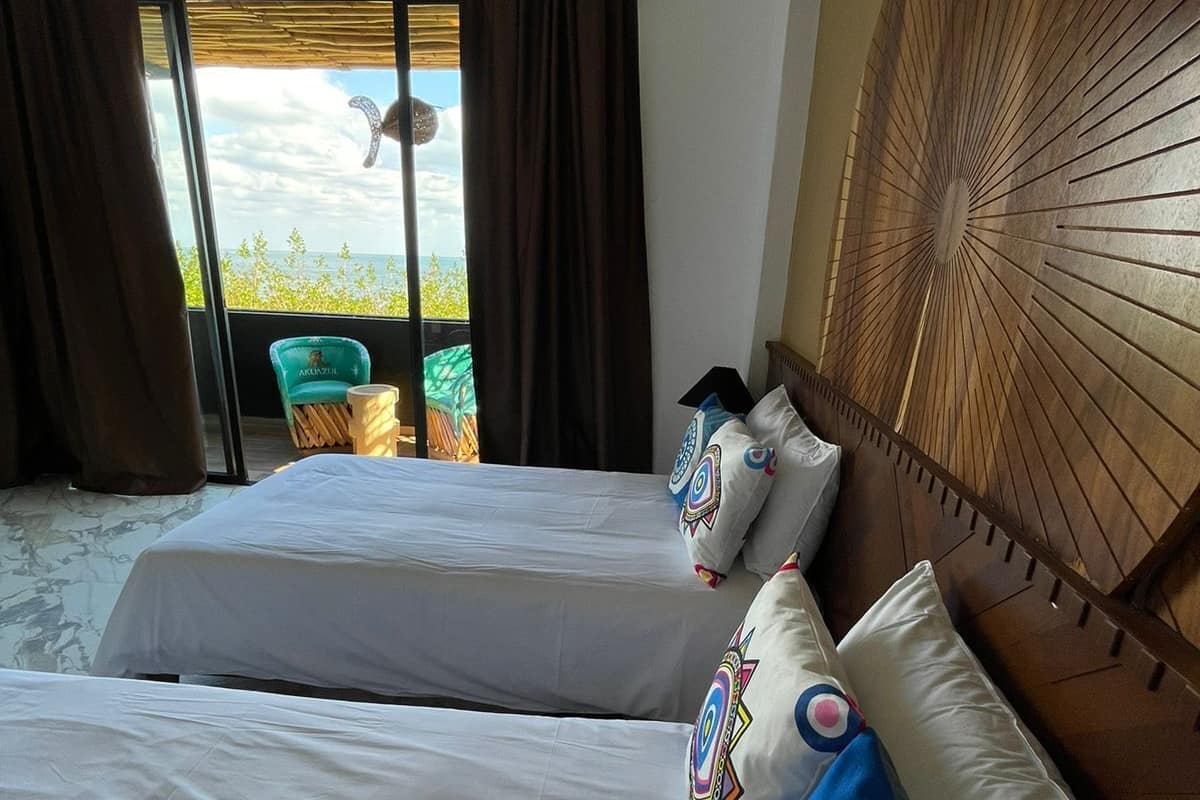 Een hotelkamer met twee bedden, uitzicht op zee en een balkon met een stoel.