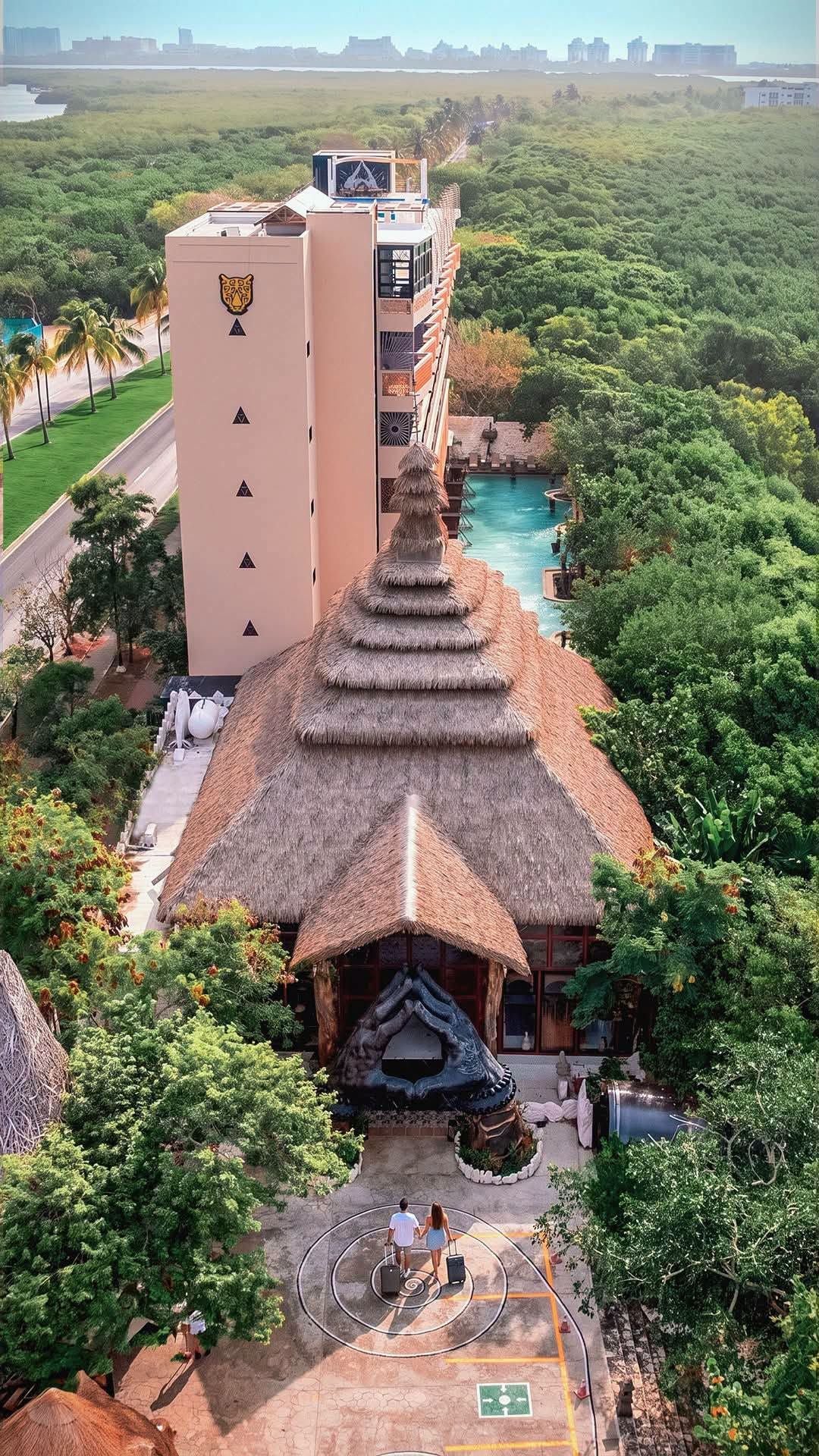 Un resort con una construcción de techo de paja, piscina y vista al horizonte de la ciudad.