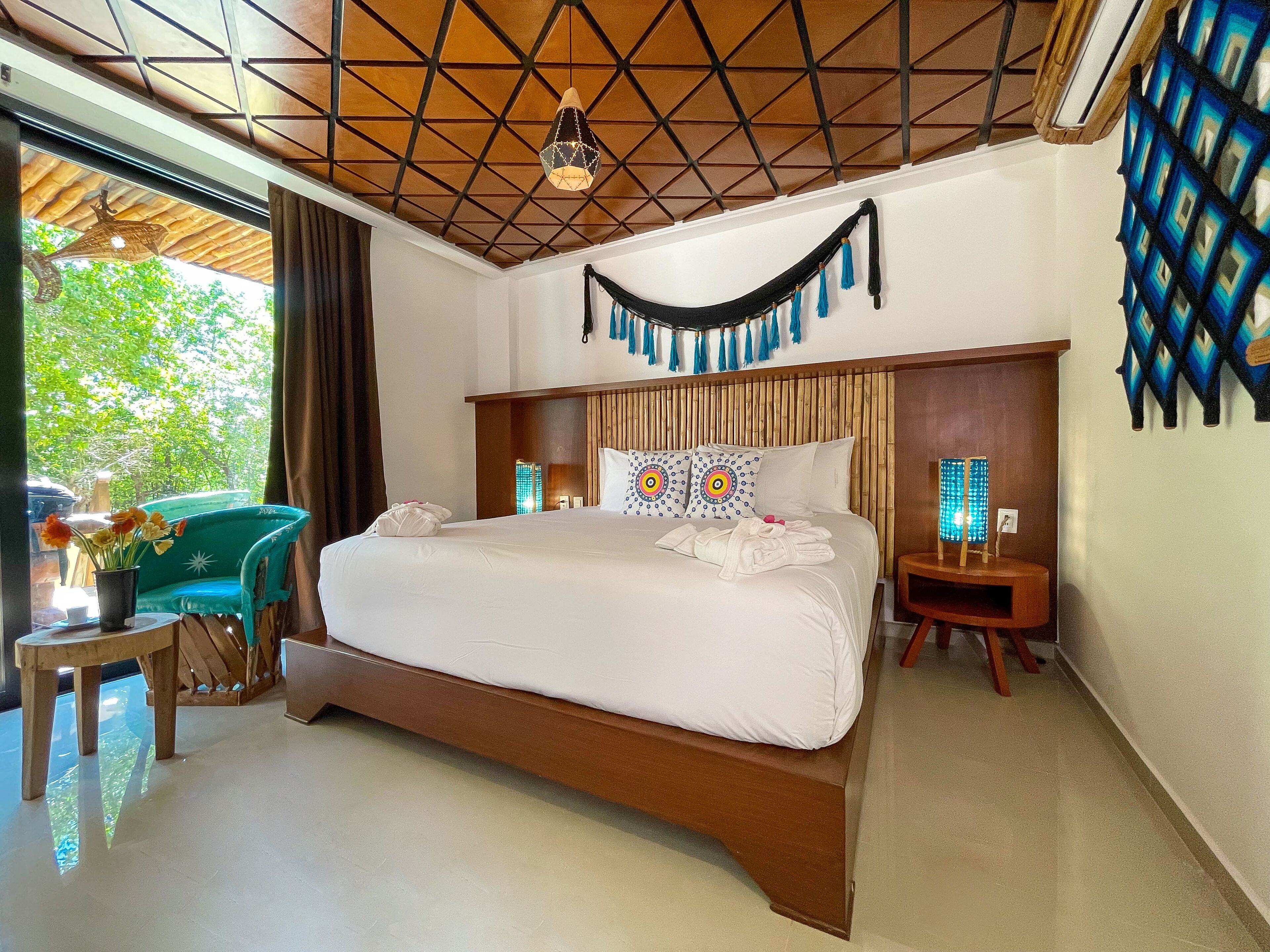 A hotel room with a large bed, wooden headboard, and a view of greenery outside.