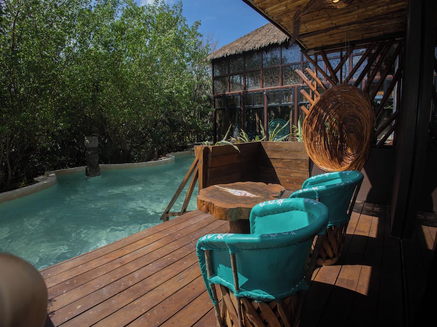 Une terrasse en bois avec une piscine, des chaises turquoise et une structure surmontée d’un toit de chaume.