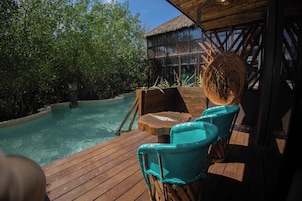 Una terraza de madera con piscina, sillas turquesas y una estructura de techo de paja.
