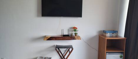 Una sala de estar moderna con un televisor de pantalla plana montado en la pared, un estante de madera con una planta pequeña, un refrigerador compacto y una silla plegable elegante.