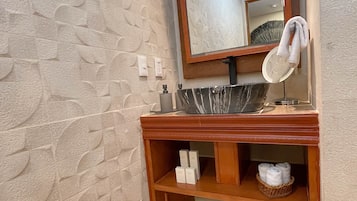 Un baño con lavamanos de mármol, tocador de madera y pared con textura.