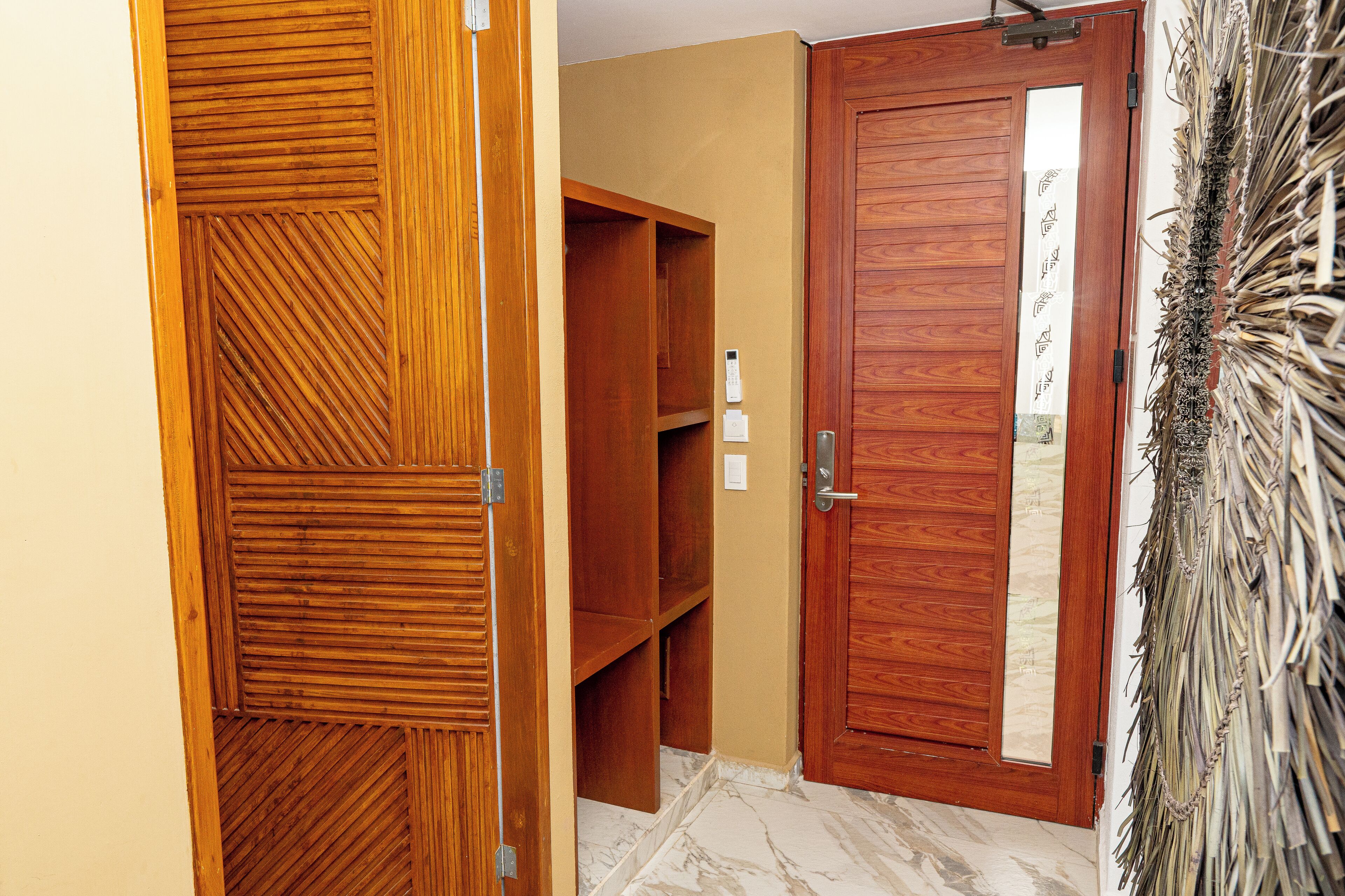 Une porte en bois avec un panneau de verre, une étagère en bois et une plante décorative fixée au mur.