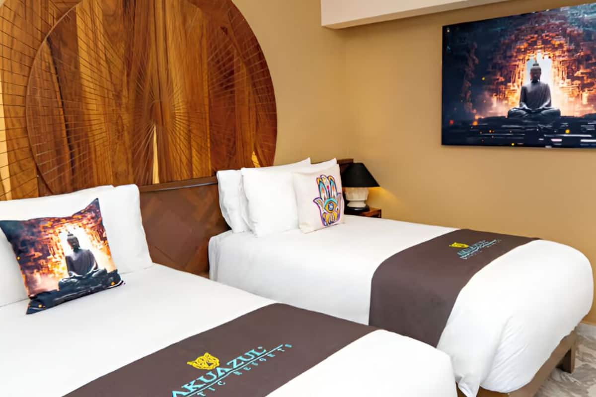Een hotelkamer met twee bedden, een groot houten hoofdeinde, een televisie aan de muur en een Boeddhabeeld.
