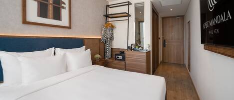 Quarto de hotel com uma cama grande, cabeceira de madeira, mesa de cabeceira com abajur, espelho e um quadro emoldurado na parede.